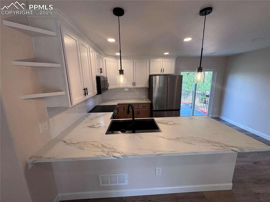 Image 10 of 36: Kitchen featuring a peninsula, freestanding refrigerator, white cabinetry,