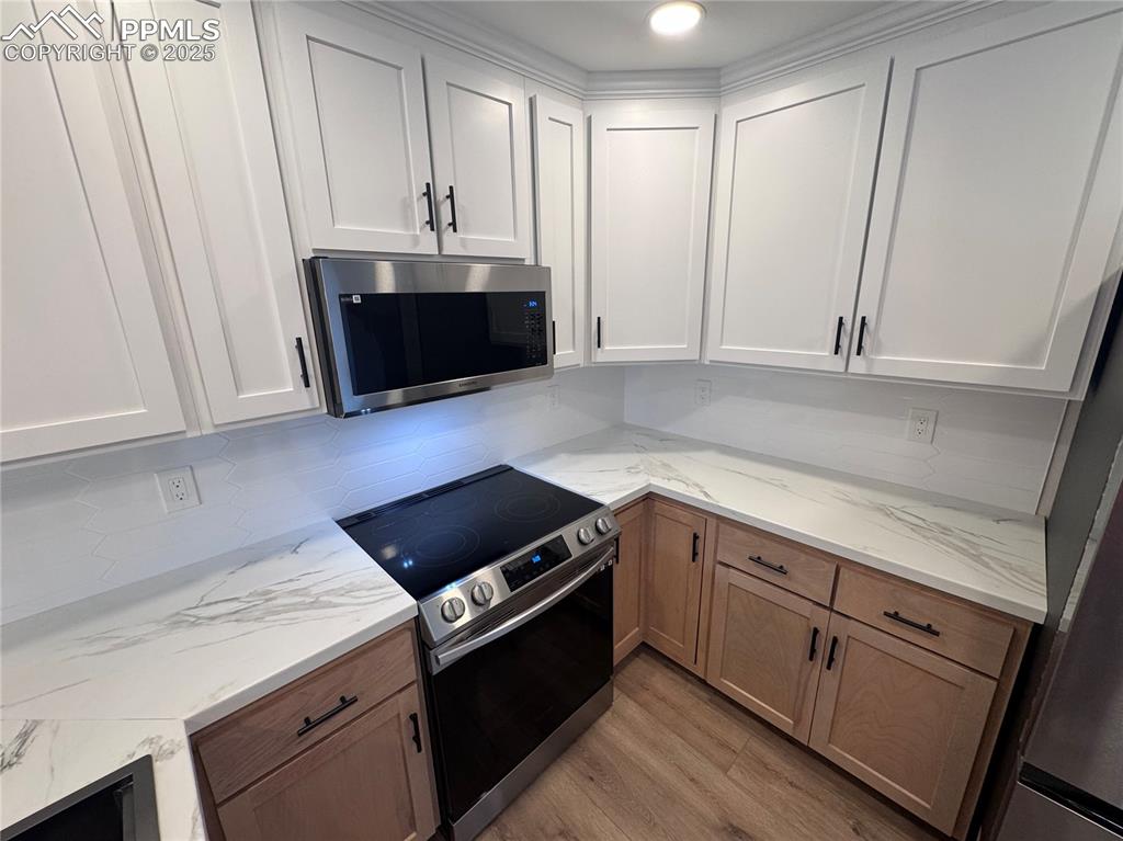 Image 8 of 36: Kitchen featuring stainless steel appliances, white cabinetry, tasteful bac