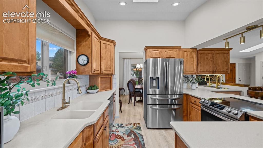 Image 22 of 50: Kitchen featuring wood cabinetry, light countertops, dual basin sink with b