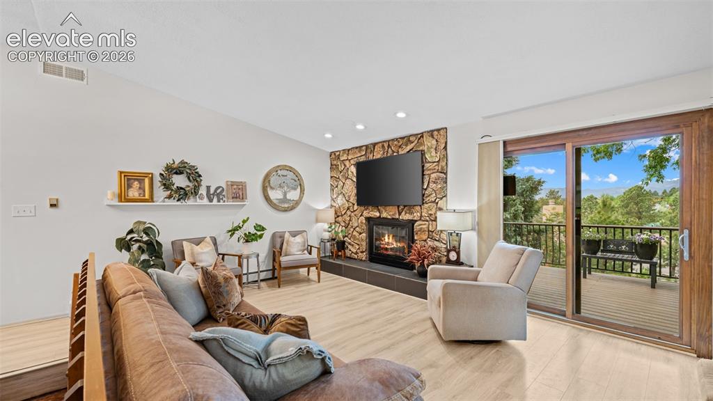 Image 26 of 50: Living area featuring light wood-finish flooring, a stone-accented fireplac