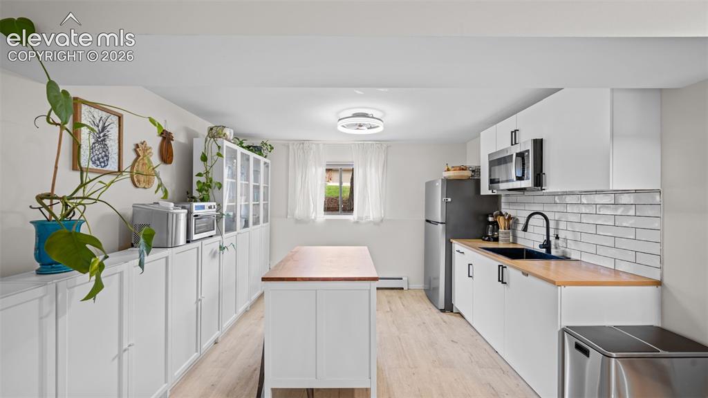 Image 28 of 50: Modern kitchen area featuring white cabinetry, light wood-finish flooring, 