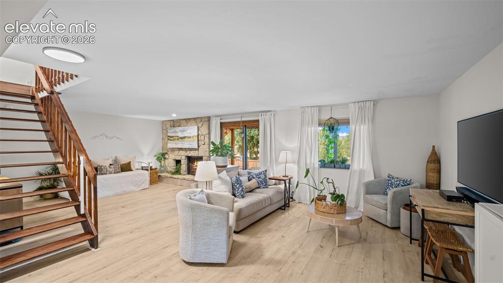Image 30 of 50: Spacious living area featuring light wood-finish flooring, a stone fireplac