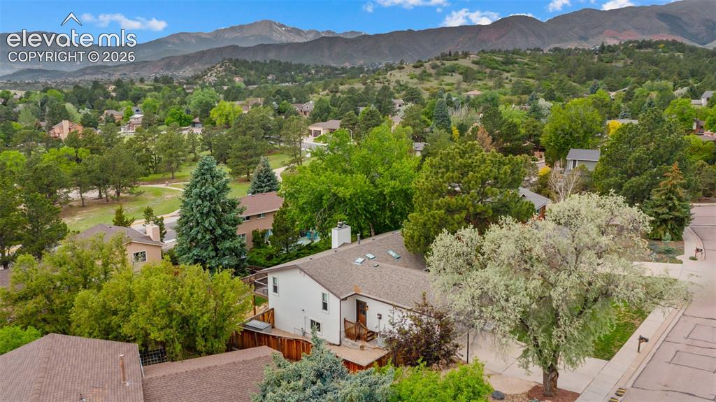 Image 43 of 50: Residences nestled among mature trees with distant mountains and a blue sky