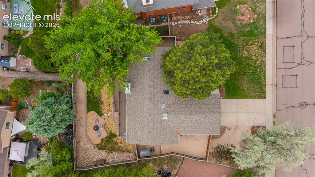 Image 46 of 50: Aerial property view featuring a shingle roof, mature trees, concrete drive