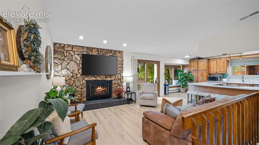 Image 9 of 50: Open-concept living space featuring a stone-accented fireplace, light wood-