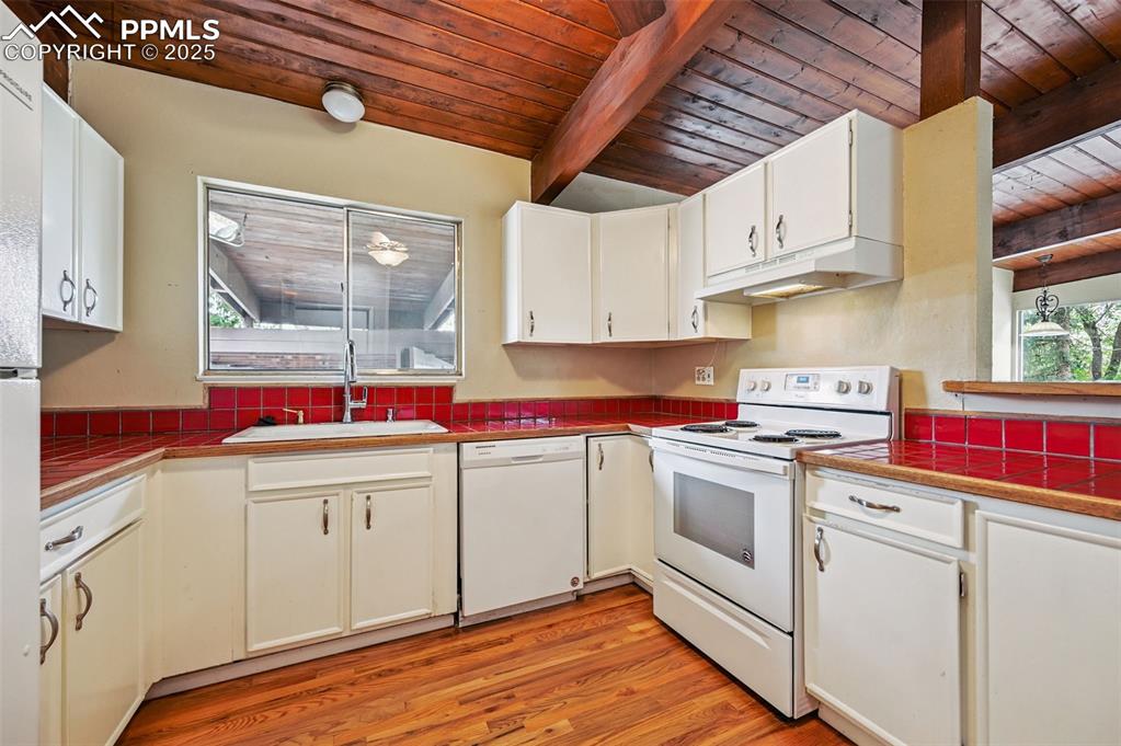 Image 12 of 44: Kitchen w/wood ceiling and exposed beams, white appliances, wood floors, un
