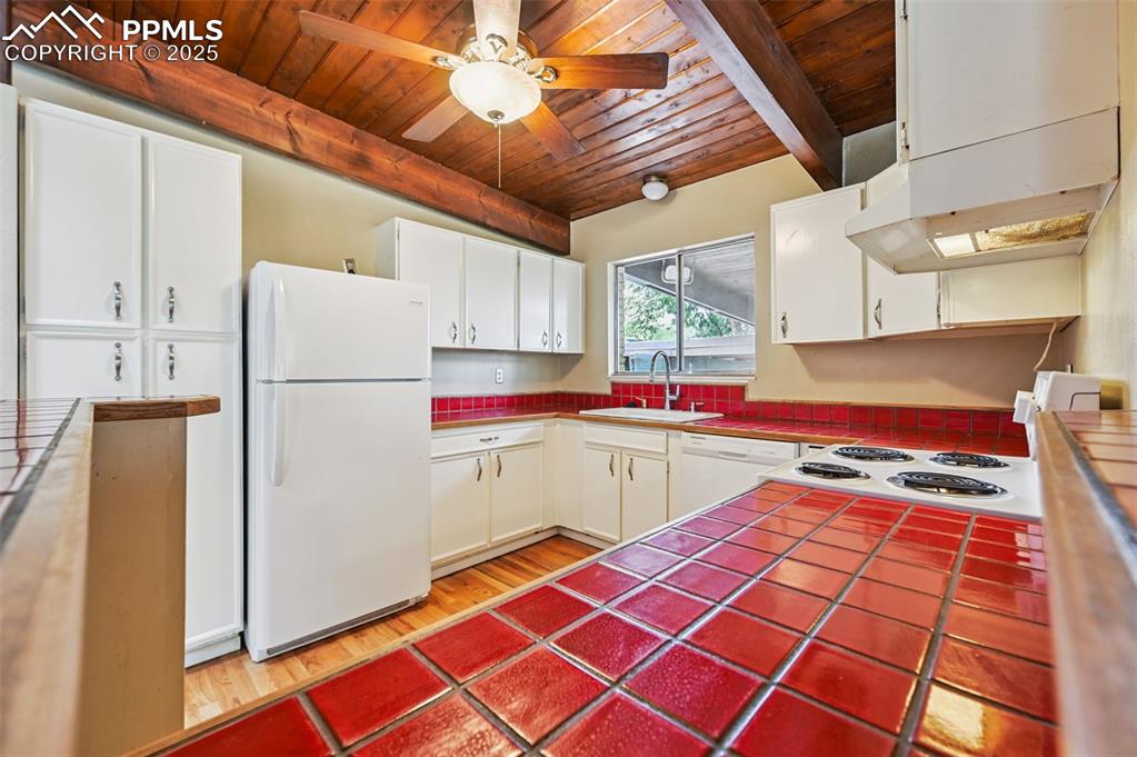 Image 13 of 44: Kitchen w/ tile counters, a wood ceiling with exposed beams, white applianc