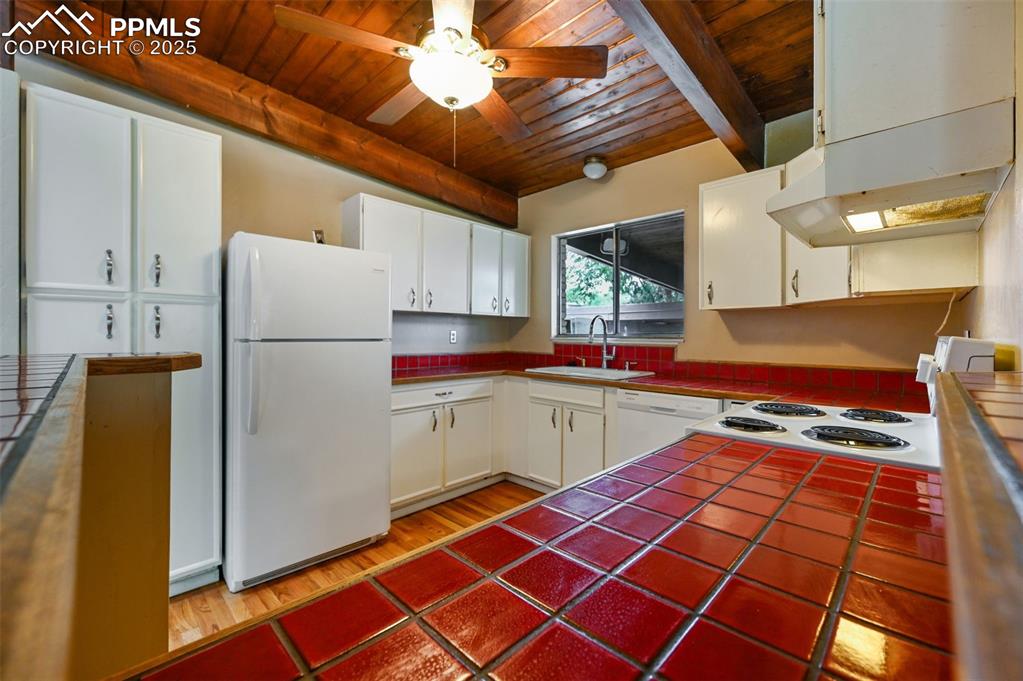 Image 14 of 44: Kitchen featuring tile counters, a wood ceiling with exposed beams, white a