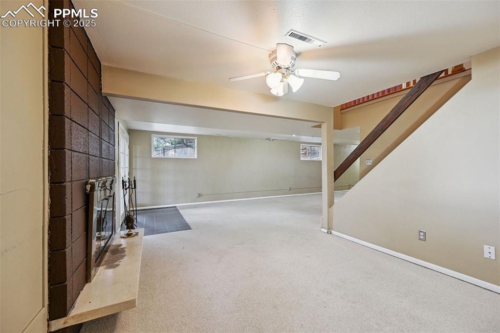 Image 21 of 44: Basement featuring carpet flooring, stairway, ceiling fan, and a large fire