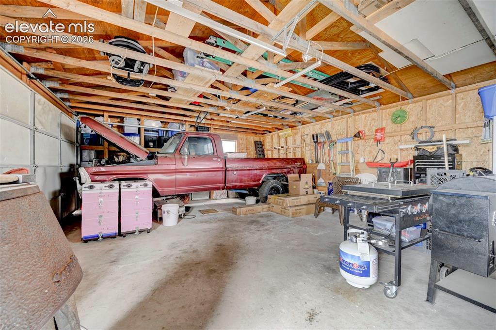 Image 30 of 36: Garage interior featuring exposed wooden rafters, concrete flooring, and am