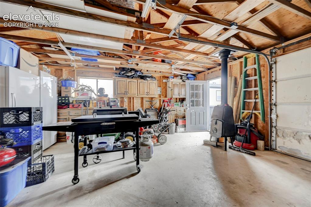 Image 31 of 36: Garage space featuring exposed ceiling joists, wood panel walls, concrete f