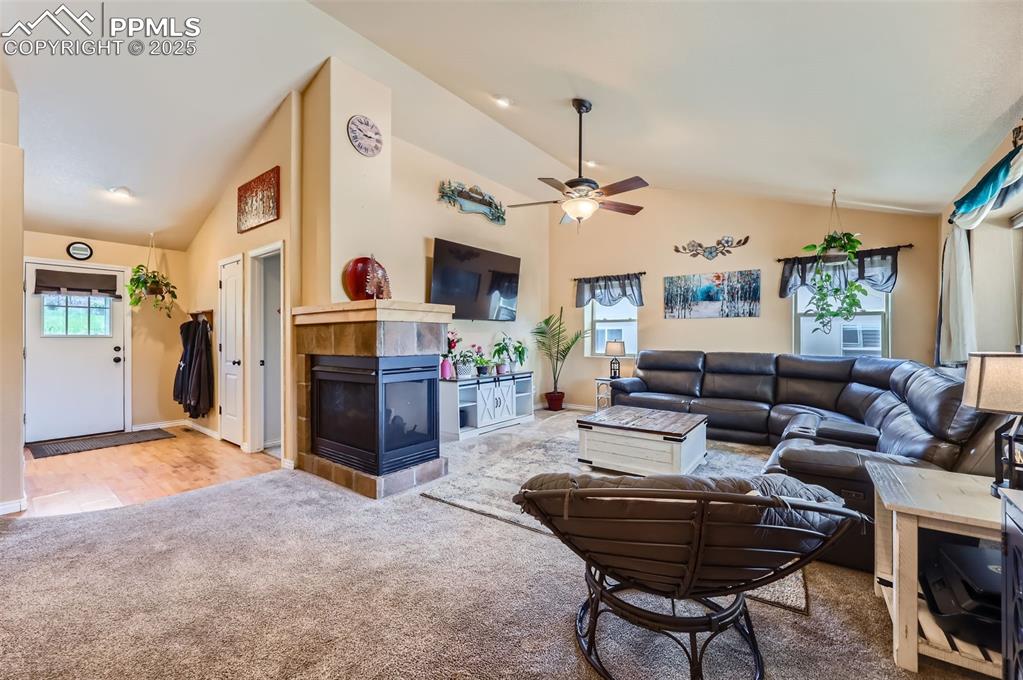 Image 6 of 29: Living room with a fireplace, carpet flooring, ceiling fan, and high vaulte