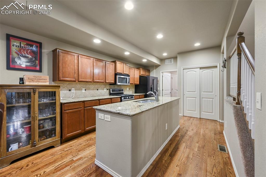 Image 10 of 50: Kitchen with stainless steel appliances, light wood-style floors, brown cab