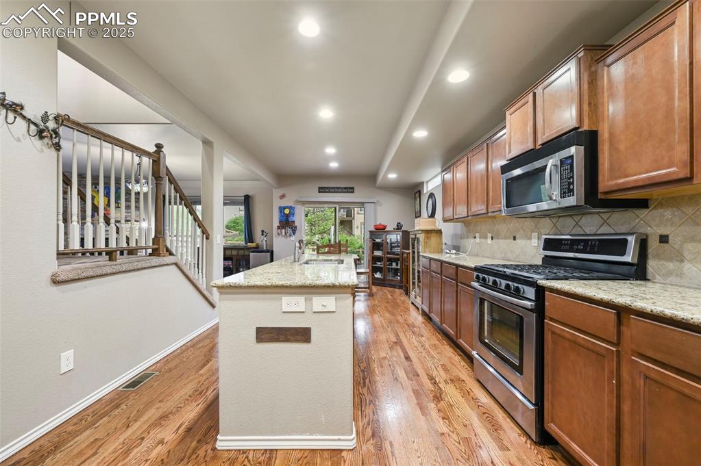 Image 12 of 50: Kitchen with stainless steel appliances, an island with sink, light wood-ty