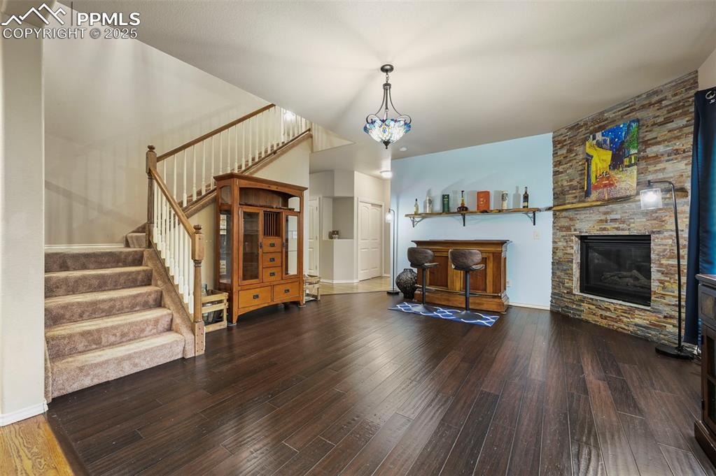 Image 16 of 50: Living room with stairs, wood finished floors, and a stone fireplace