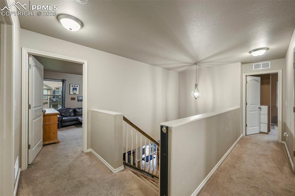 Image 18 of 50: Hall with an upstairs landing, carpet floors, and a textured ceiling