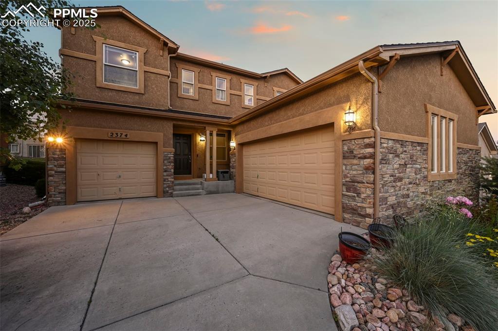 Image 3 of 50: View of front facade with stone siding, stucco siding, concrete driveway, a