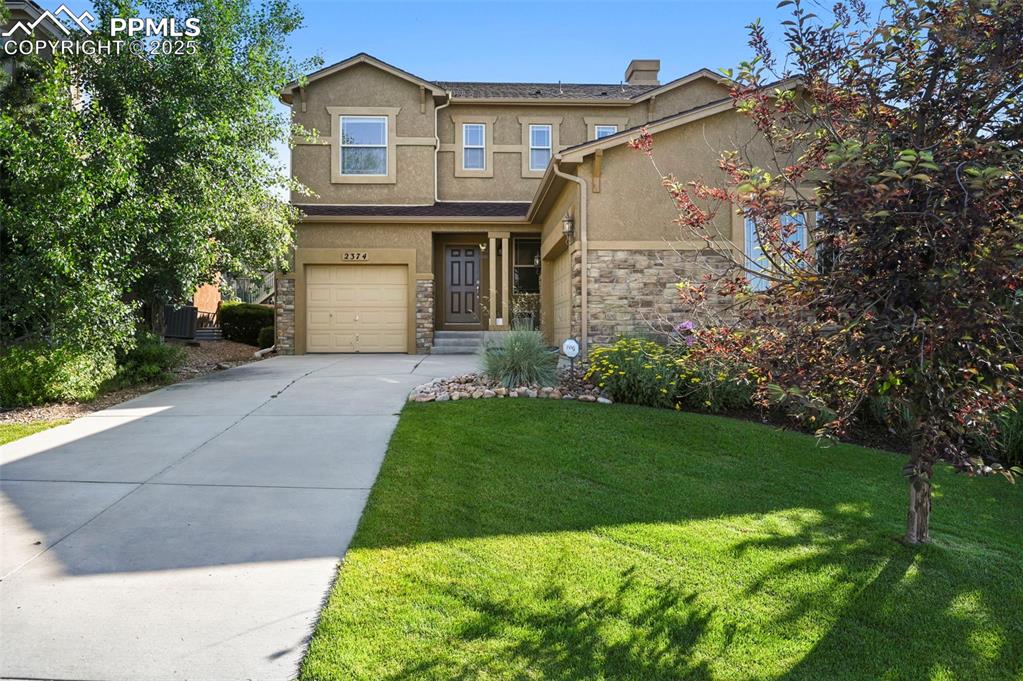 Image 4 of 50: Traditional-style house with stucco siding, stone siding, a front yard, a g
