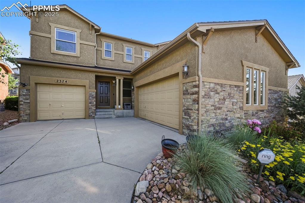 Image 5 of 50: View of front of house with stucco siding, stone siding, driveway, and an a