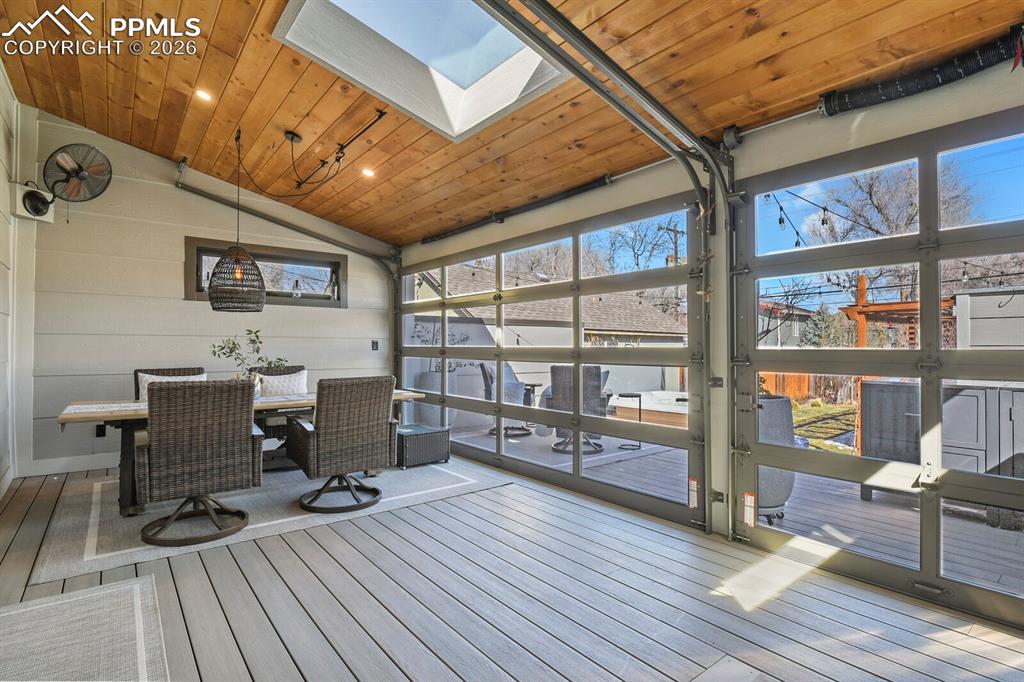Image 34 of 50: Enclosed back patio with wood ceiling, skylight, garage doors, and composit