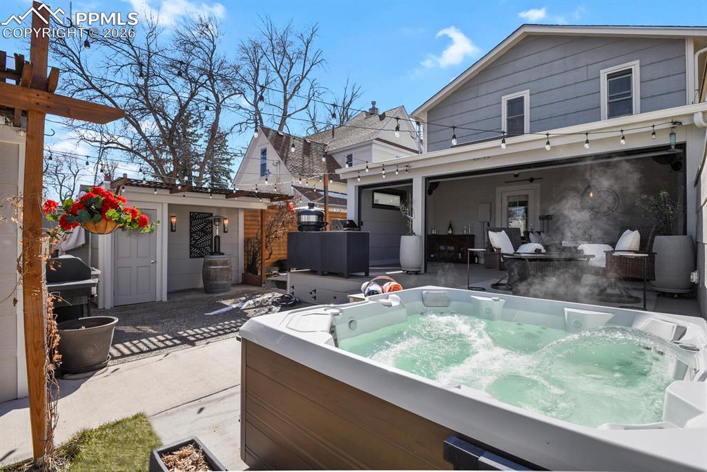 Image 39 of 50: Back pattio with the roller doors up and hot tub 