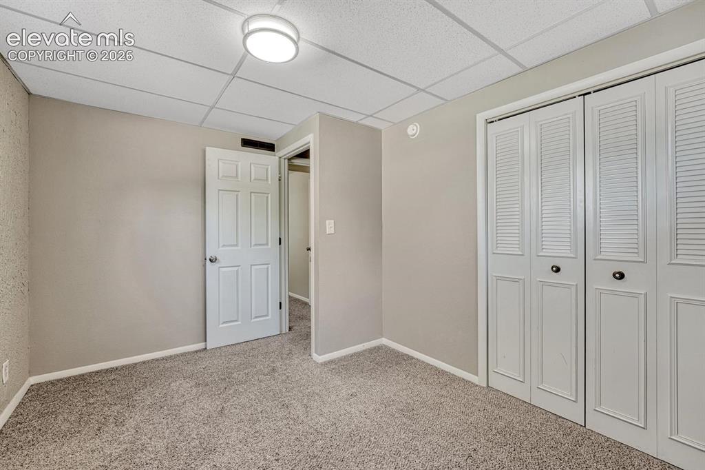Image 21 of 29: Carpeted room featuring a drop ceiling, flush-mount lighting, louvered bi-f