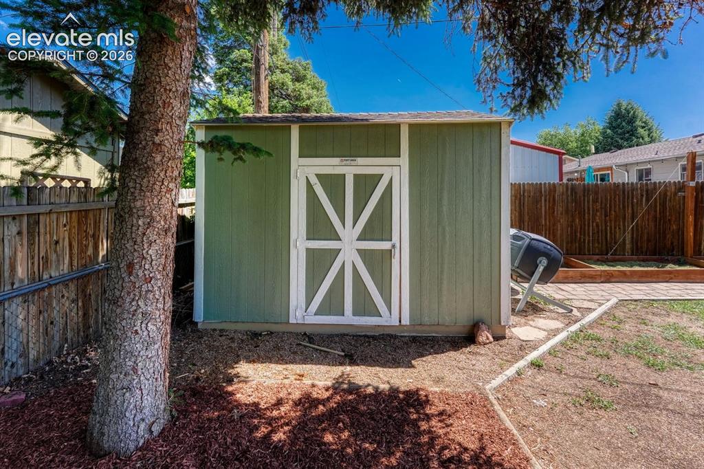 Image 27 of 29: Green storage shed featuring a white barn-style door, wood plank siding, an