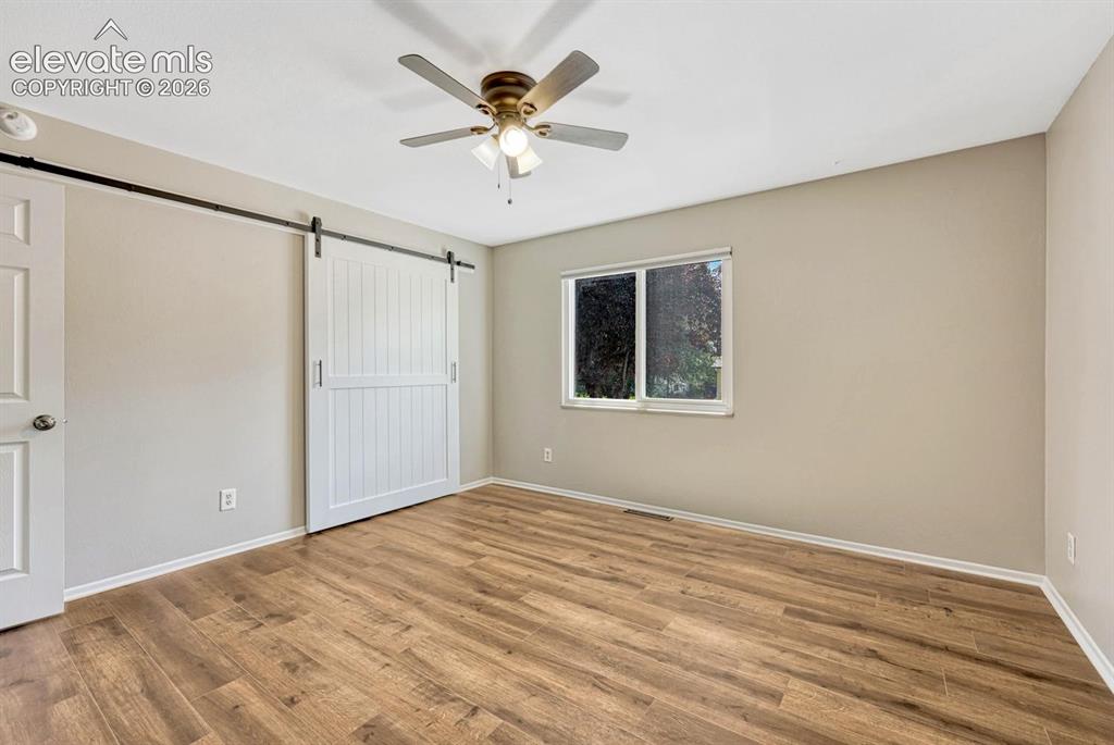Image 9 of 29: Spacious room featuring wood-finish flooring, a contemporary ceiling fan wi