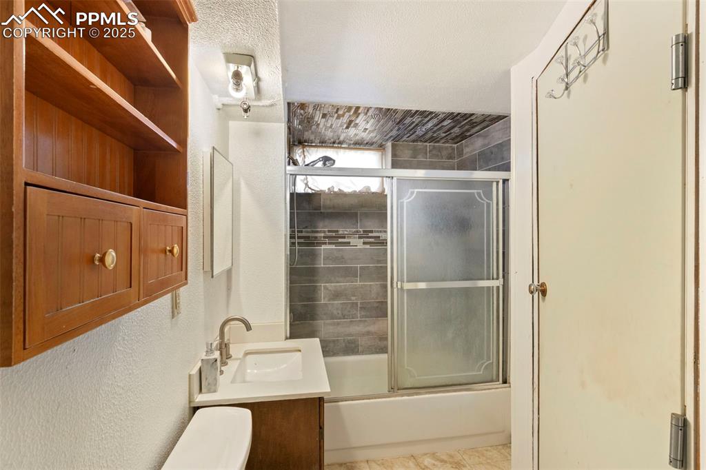 Image 19 of 25: Bathroom with vanity, shower / bath combination with glass door, a textured