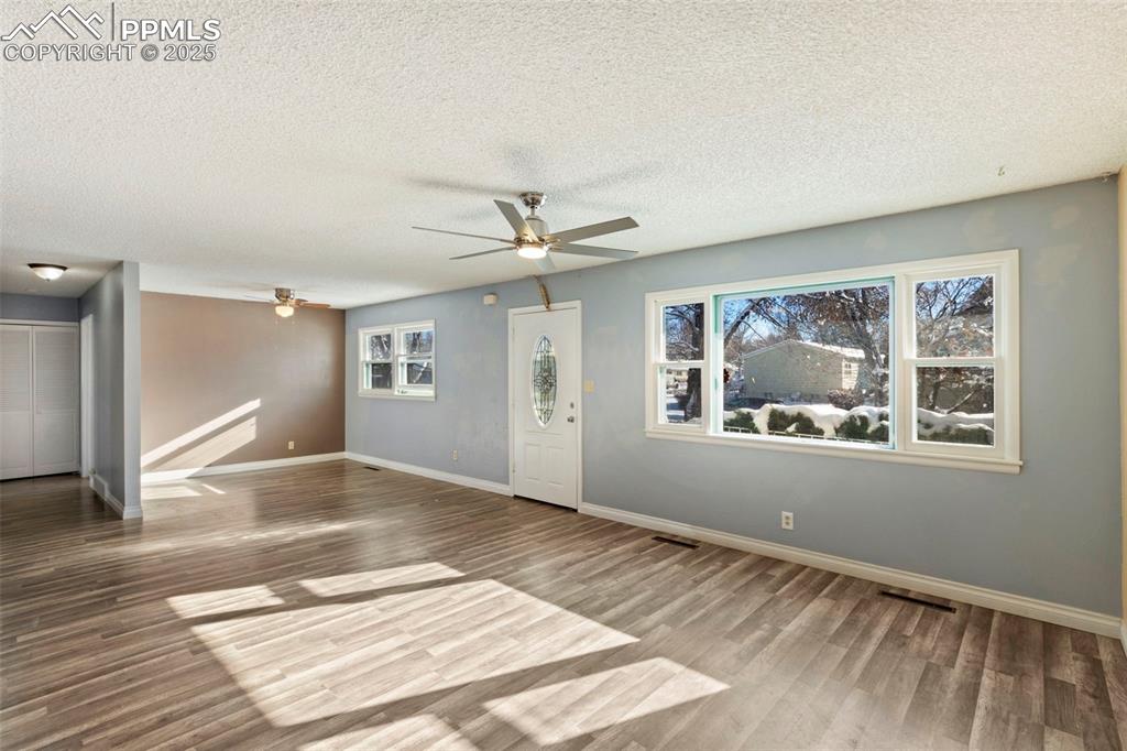 Image 4 of 25: Unfurnished living room with ceiling fan, a textured ceiling, and wood fini