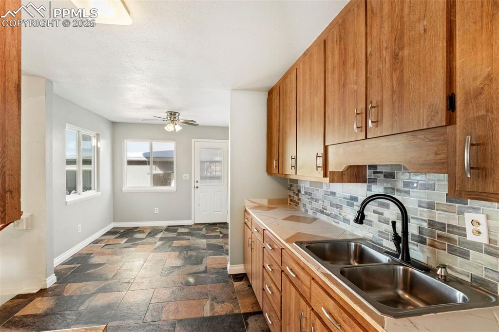 Image 6 of 25: Kitchen with brown cabinets, backsplash, light countertops, and stone tile 