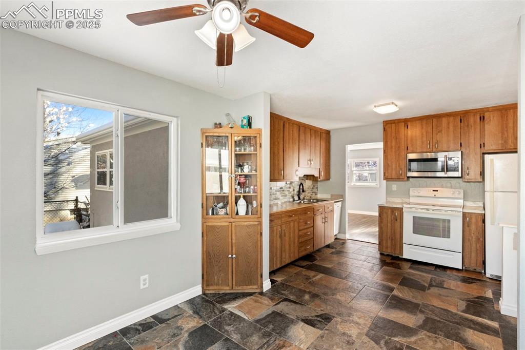 Image 8 of 25: Kitchen with white appliances, light countertops, brown cabinets, and backs