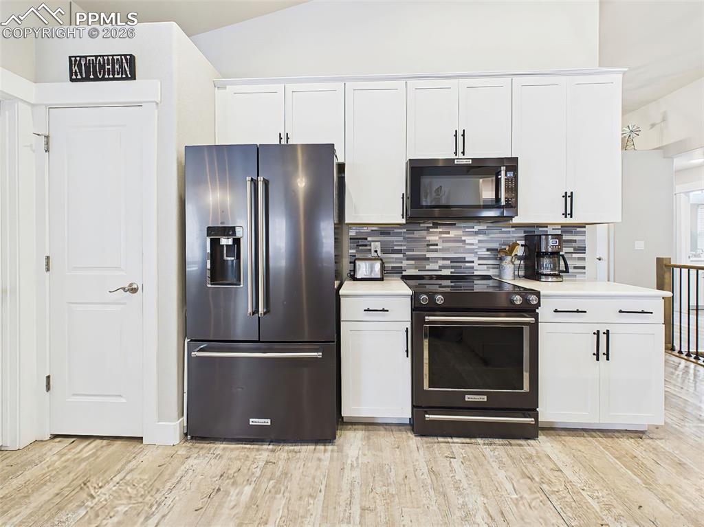 Image 10 of 50: Modern kitchen with white cabinetry, tile backsplash, and Kitchenaid applia