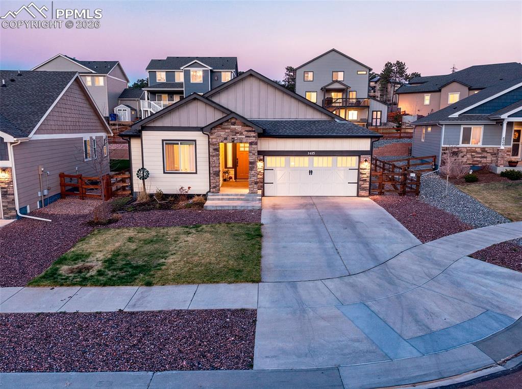Image 4 of 50: Warm exterior lighting highlights the home’s stone-accented façade, covered