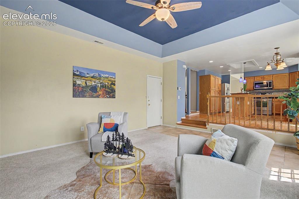 Image 12 of 42: Living room featuring a tray ceiling with a ceiling fan, carpeted flooring,