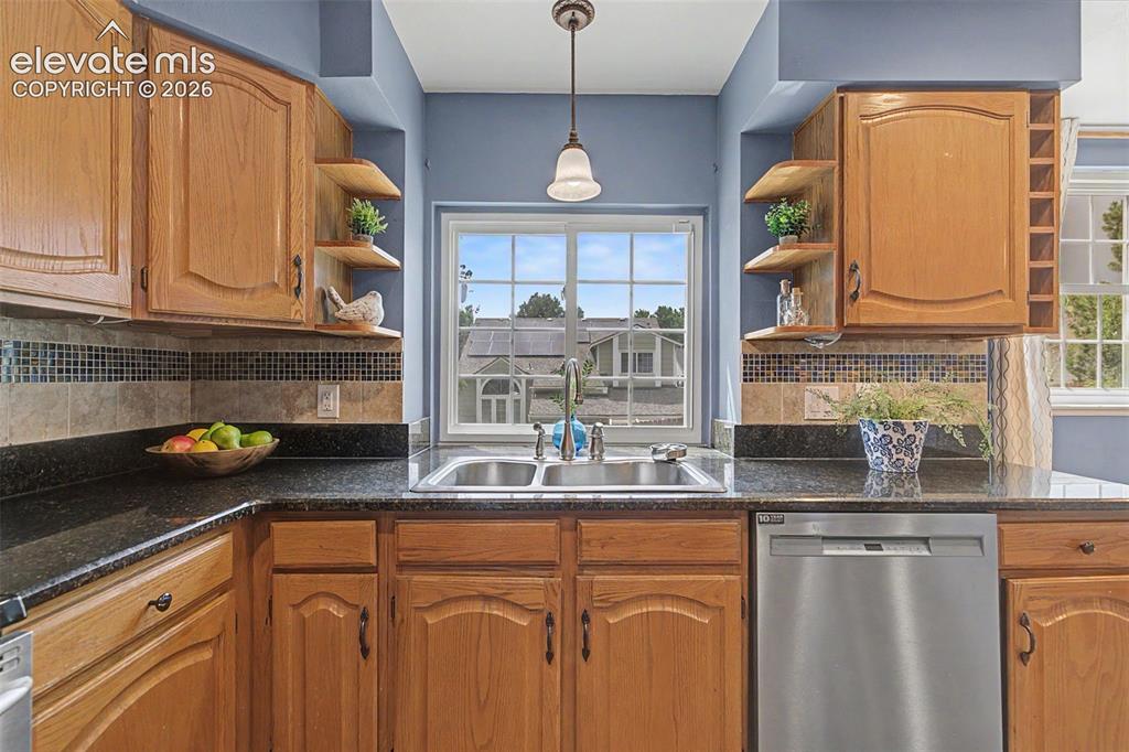 Image 14 of 42: Kitchen featuring wood cabinetry, dark speckled countertops, and a mosaic t