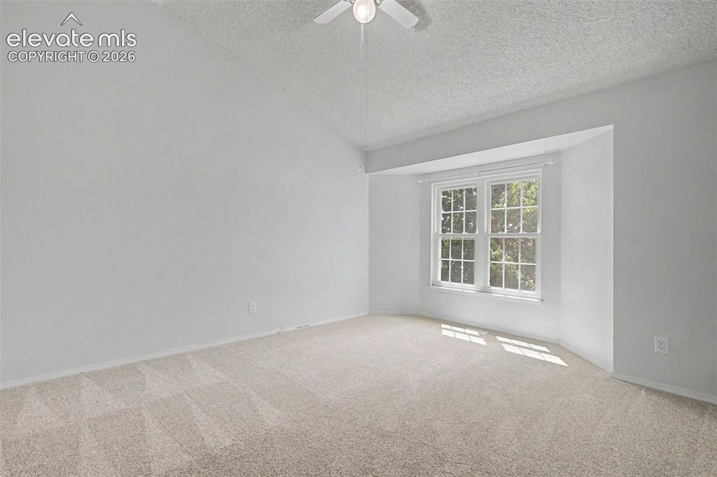 Image 27 of 42: Spacious room featuring a bay window, vaulted ceiling, and neutral carpetin