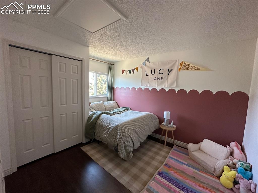 Image 12 of 14: Bedroom featuring a textured ceiling, attic access, a closet, and dark wood