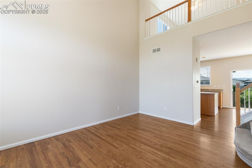 Image 4 of 45: Unfurnished room with wood finished floors, stairway, and a high ceiling