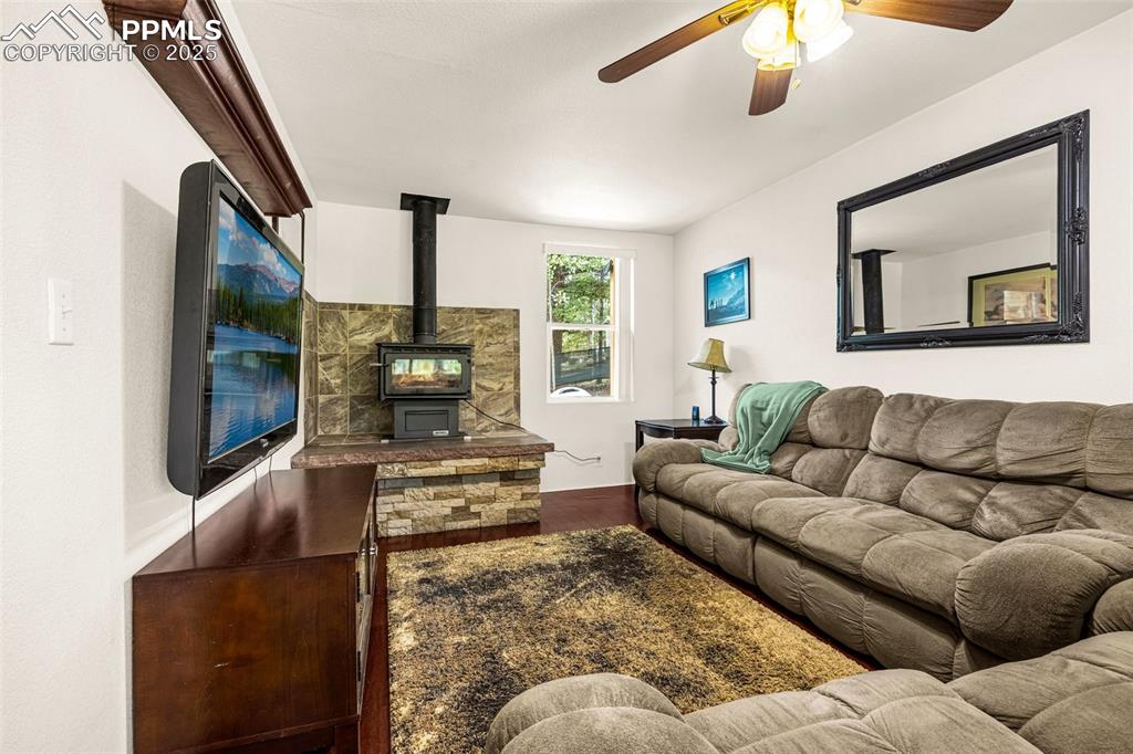 Image 10 of 31: Living room featuring wood finished floors, a wood stove, and a ceiling fan