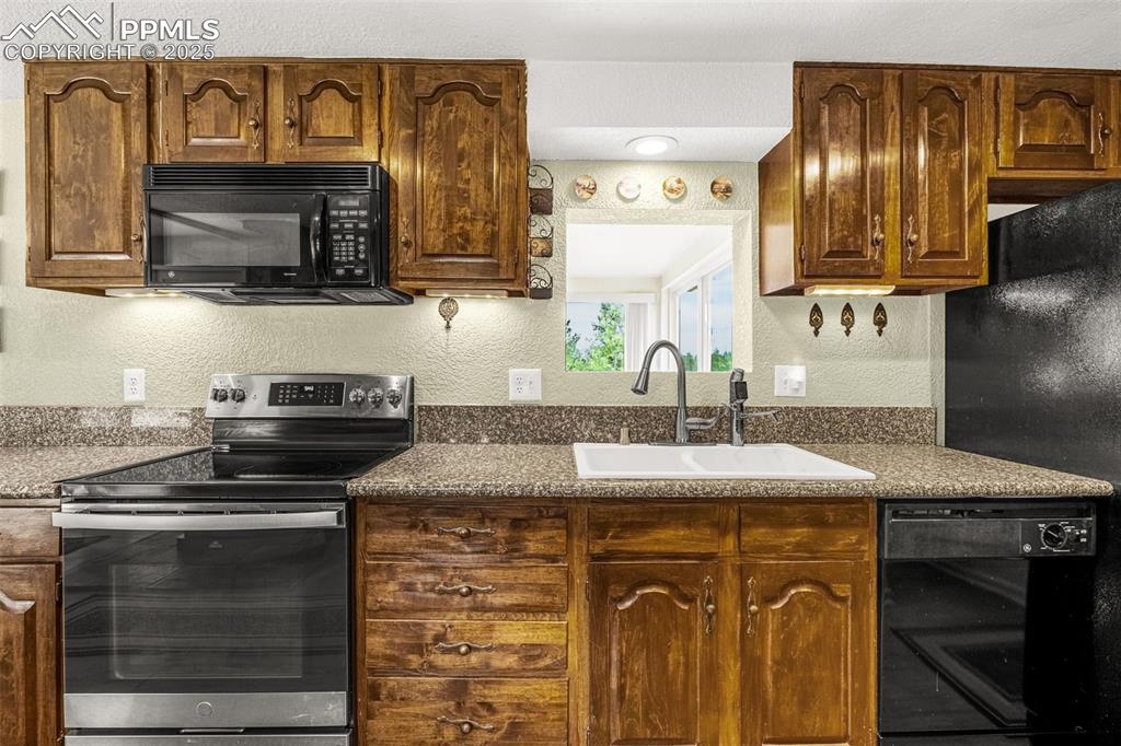 Image 8 of 31: Kitchen with black appliances, dark countertops, and a textured wall