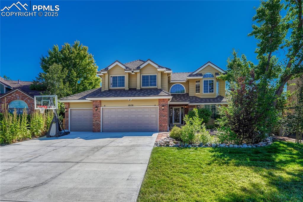 Caption: Traditional-style home with concrete driveway, brick siding, a front yard, and a garage