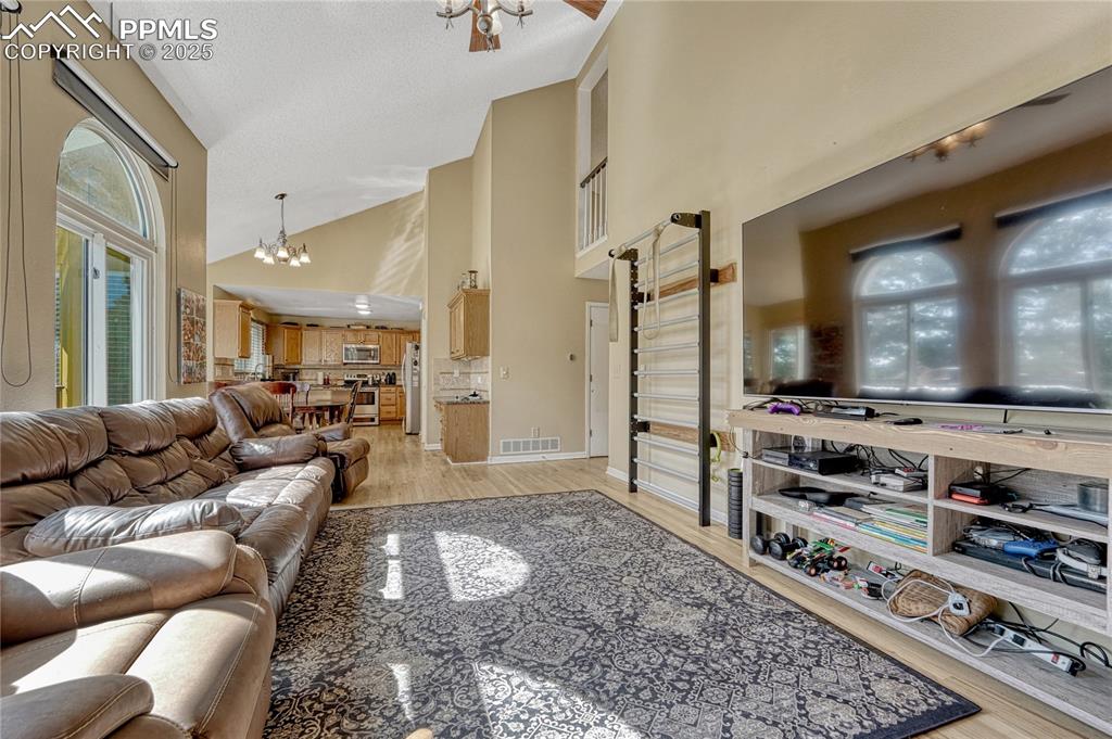 Image 16 of 31: Living room with a chandelier, light wood finished floors, and high vaulted