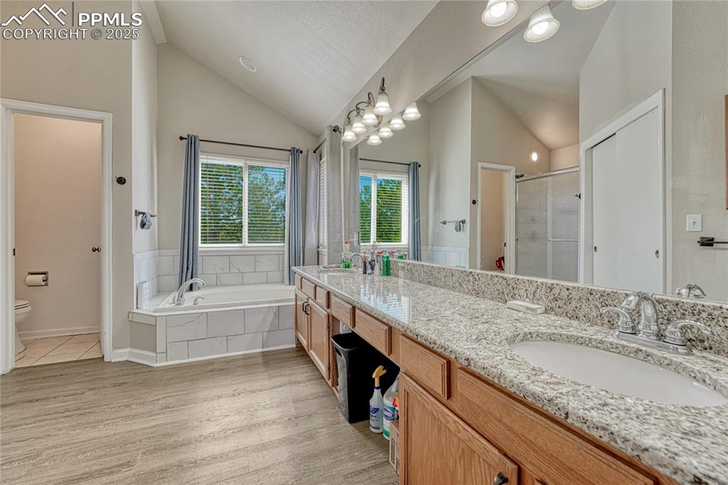 Image 20 of 31: Bathroom featuring double vanity, a shower stall, a garden tub, high vaulte