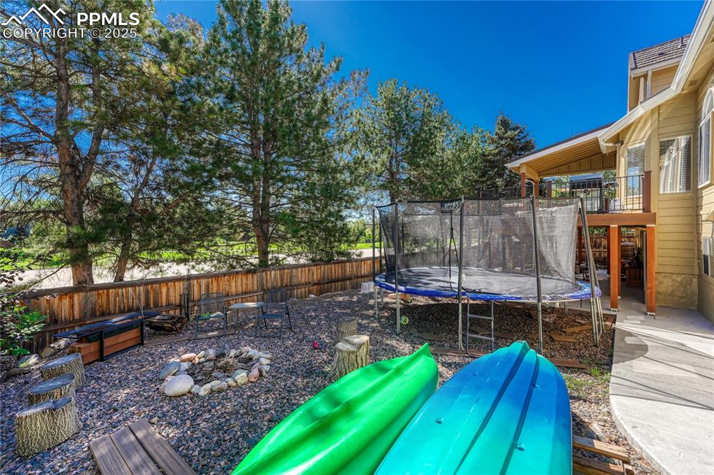 Image 31 of 31: Fenced backyard with a patio, a trampoline, and a fire pit