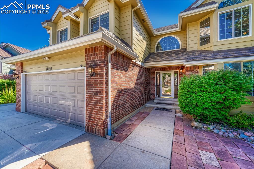 Image 5 of 31: Doorway to property with brick siding, a garage, and driveway