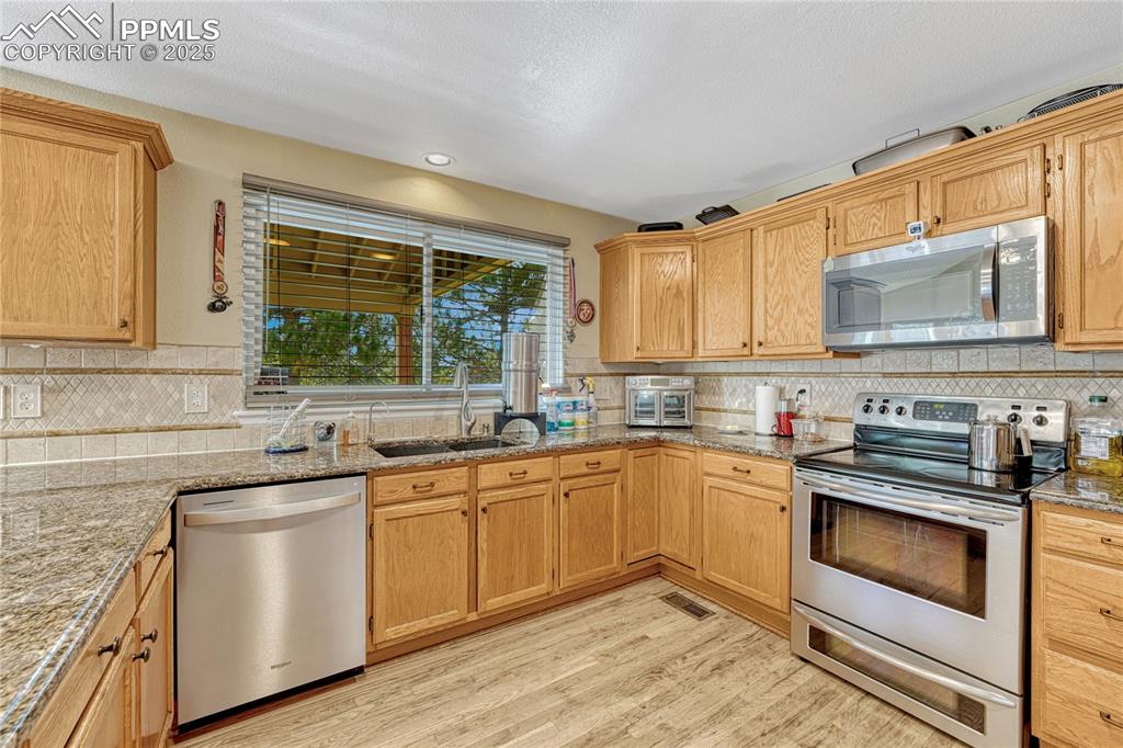 Image 7 of 31: Kitchen featuring appliances with stainless steel finishes, light stone cou