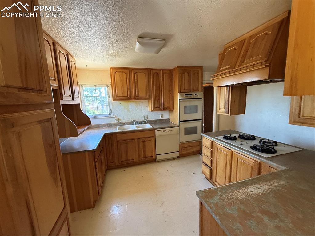 Image 11 of 23: Kitchen featuring dishwashing machine, cooktop, double oven, brown cabinets