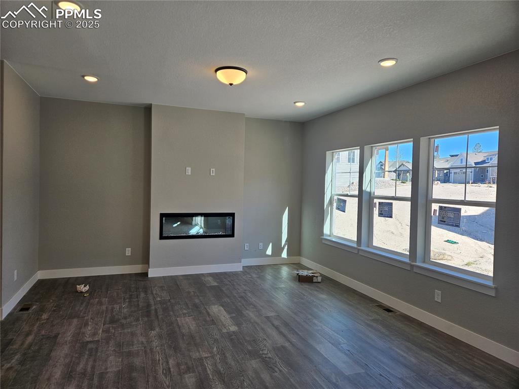 Image 4 of 12: Unfurnished living room with a glass covered fireplace, dark wood-style flo
