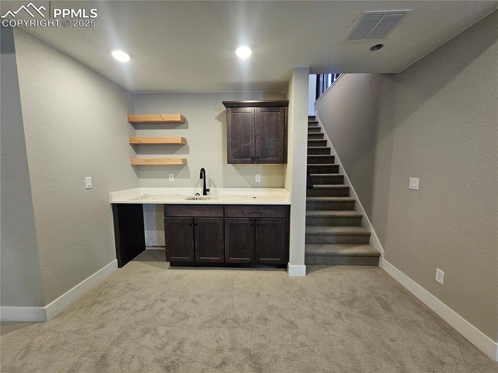 Image 8 of 12: Bar with dark brown cabinetry, a textured wall, open shelves, light colored